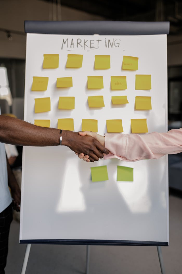 ours-journey Colleagues shaking hands in front of a marketing board during a business meeting.